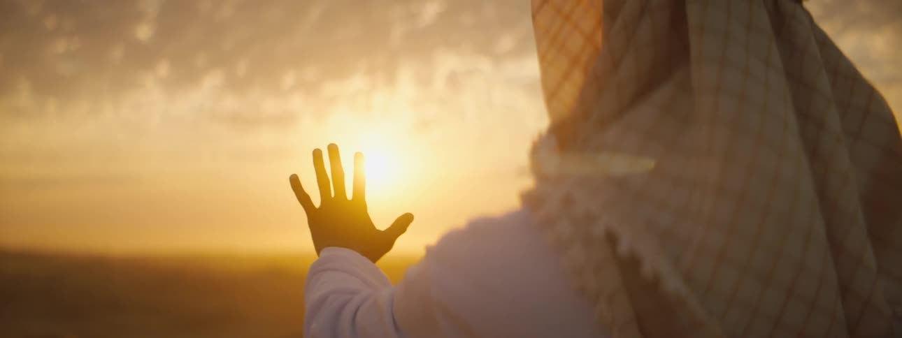 A person standing in the desert holds their hand up to the sun