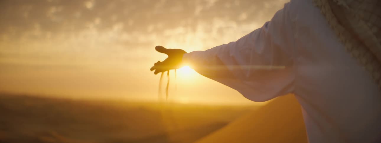 A person with a handful of sand in a desert at sunset