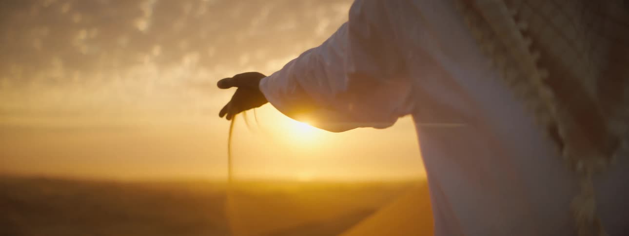 Middle eastern man picks up sand in the desert and lets it fall through his fingers back onto the ground