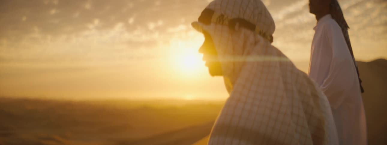 Two men watch the sunset in the desert