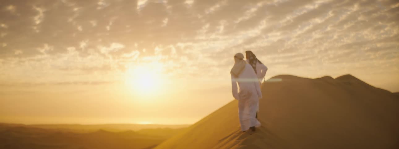 Two people hike up the dune in the desert