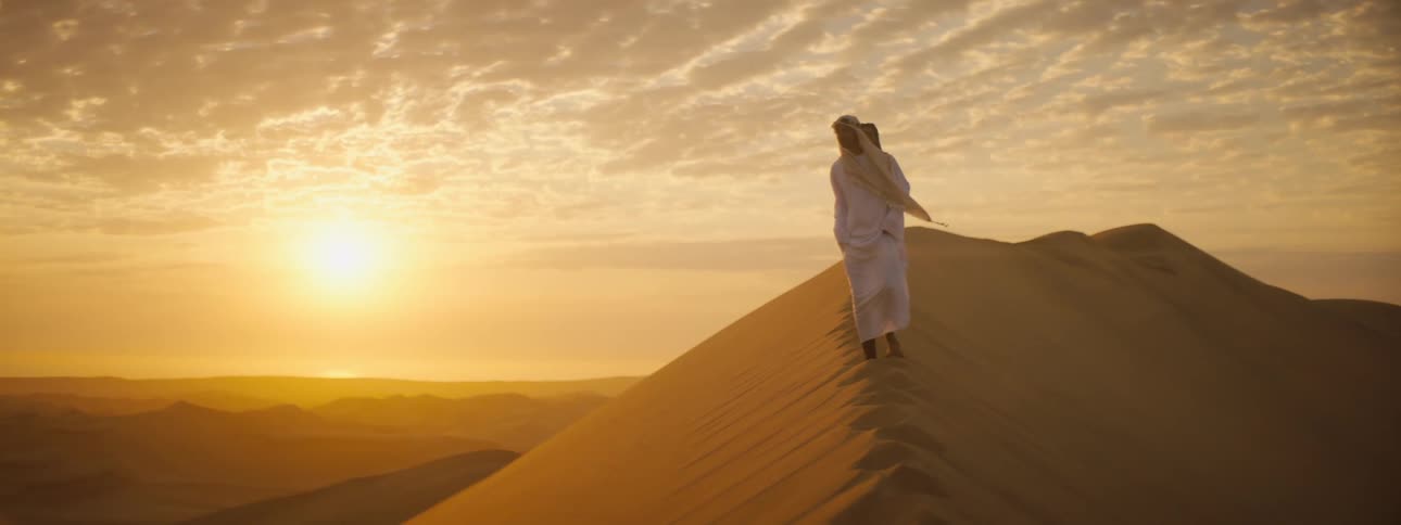 Two people walking on a sand dune in a desert at sunset