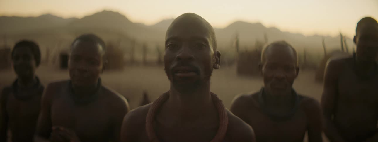 A group of shirtless tribal men standing together outdoors while looking into the camera