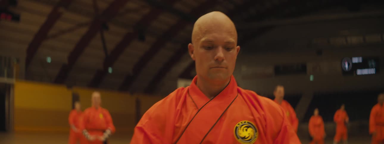 A large group of people in orange uniforms perform karate moves in a class in a gym
