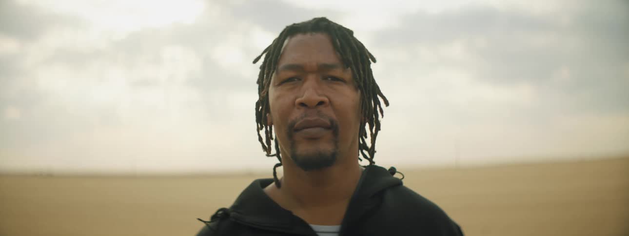 Man with a goatee and braids stares at the camera