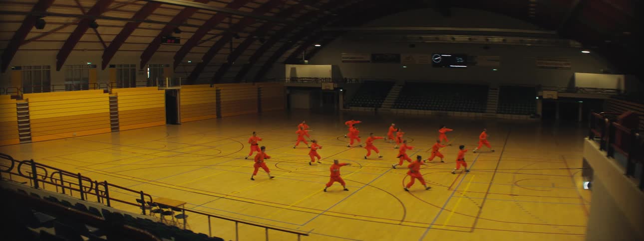 A group of people in red clothing practice martial arts forms in unison in a gymnasium