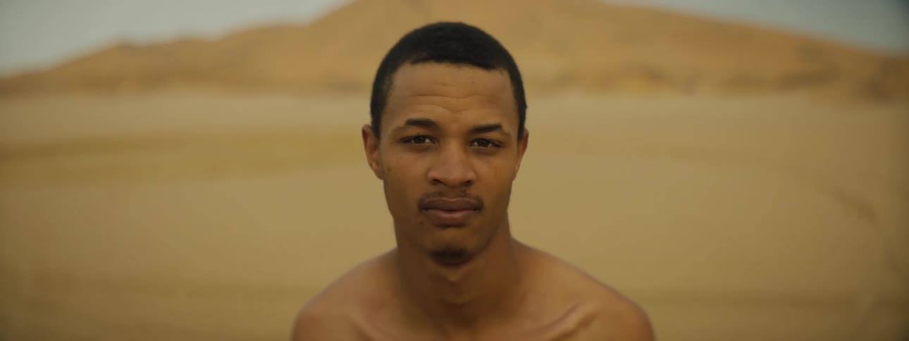 Bare chested man stands on sands near hill
