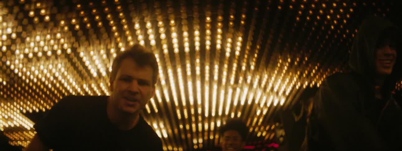 Four men are dancing in unison under a ceiling with flashing lights while wearing black clothes