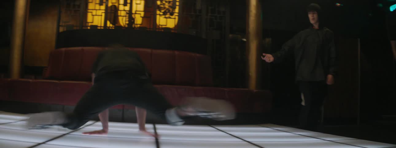 A group of men split apart to make room for a man to break dance and pose on the glowing dance floor