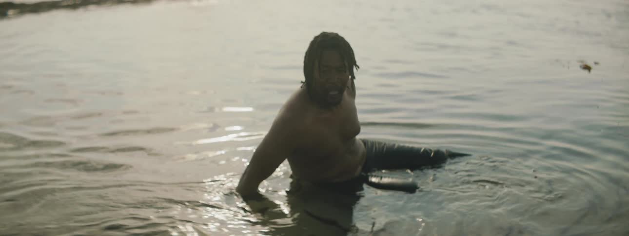 A man wearing jeans sits in a lake and nervously looks around