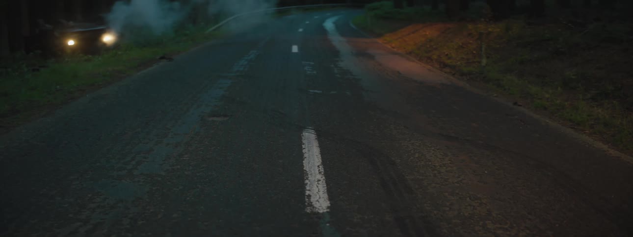 Smoke floating away from a car accident on the side of a road at night