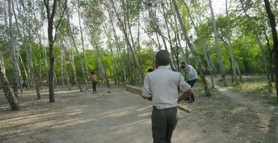Boys playing cricket as a man films
