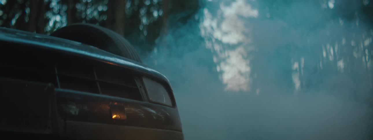 Smoke billows from an overturned vehicle in a woodland during the day