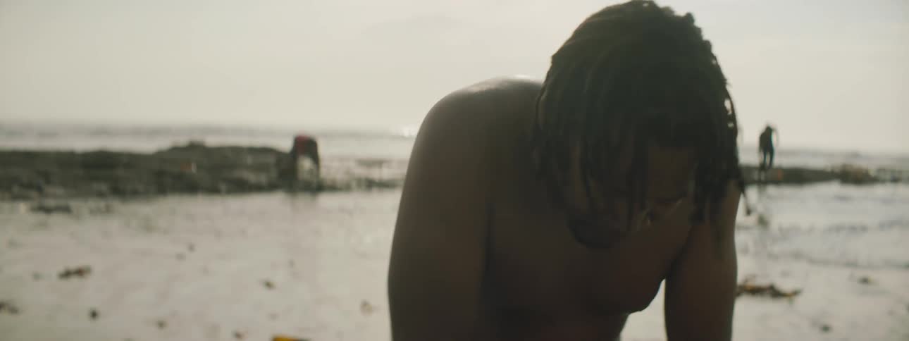 Man performs cpr on person lying on beach then turns to look toward others nearer the surf