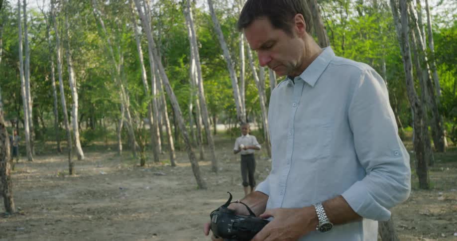 A man holds a camera as a boy throws a ball in the background