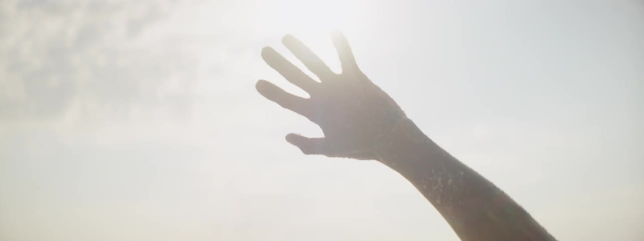 Personstanding on shore reaches up toward sun