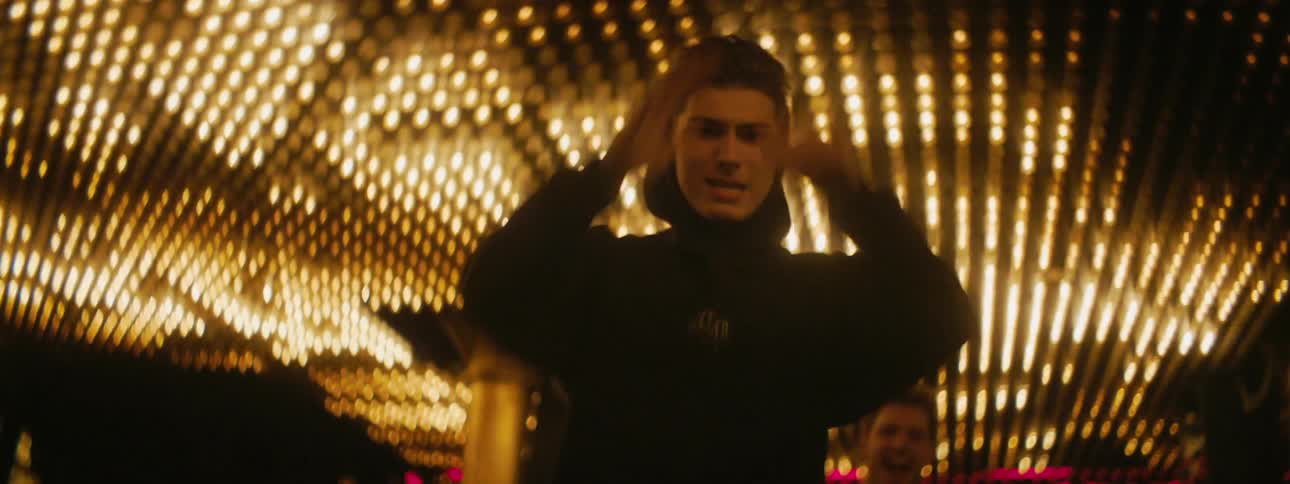A group of young men dance under a ceiling covered in an array of lights showing rapidly changing patterns