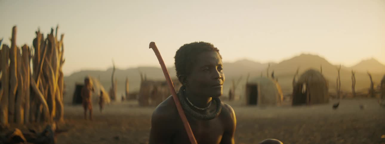 A man in a tribal clothing sits outdoors in a tribal village during the day