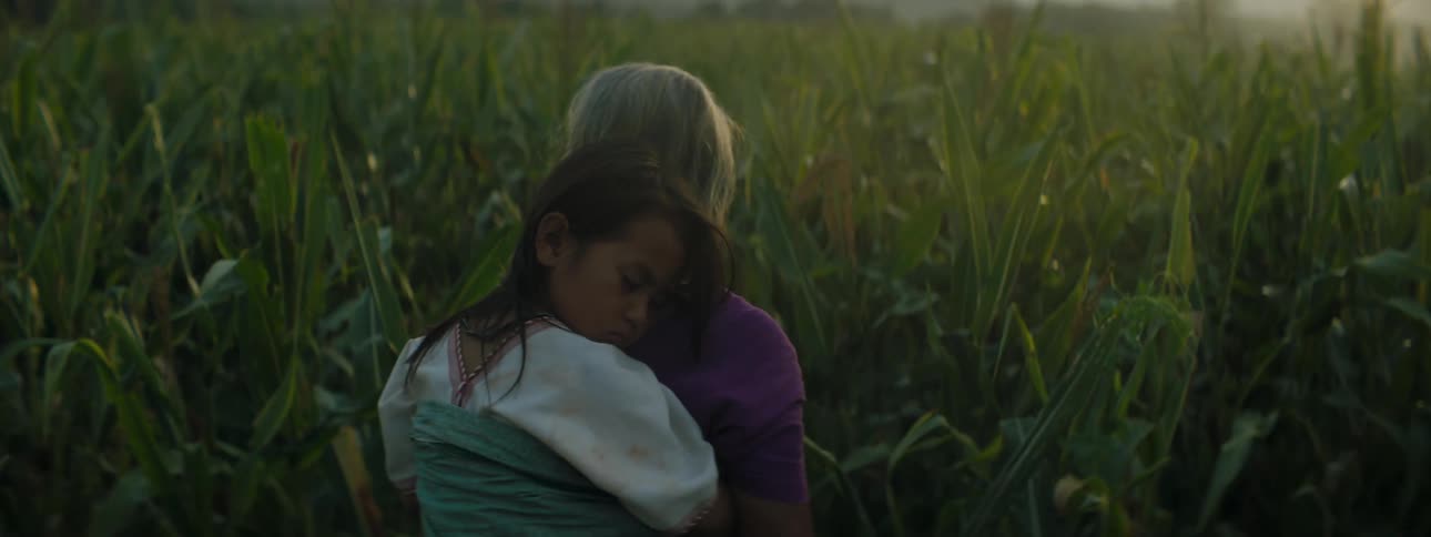A woman carries a child through the dense farm
