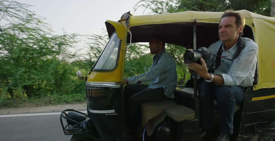 A man is holding a camera as he hangs out of a vehicle