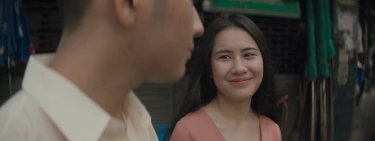 A young woman smiles at a young man as they stand together outdoors in a city during the day