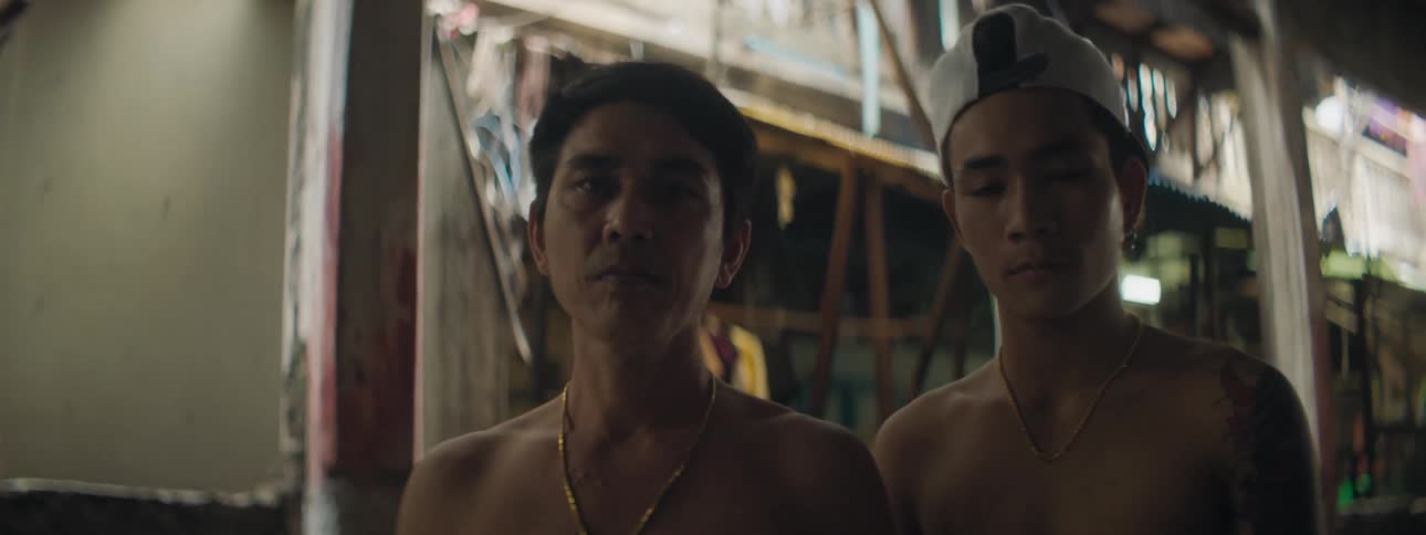 Two topless men stand near apartment building under covered walkway