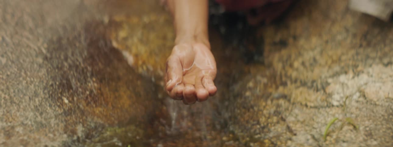 A persons where a robe using hand to scoop up water from a stream on a big rock