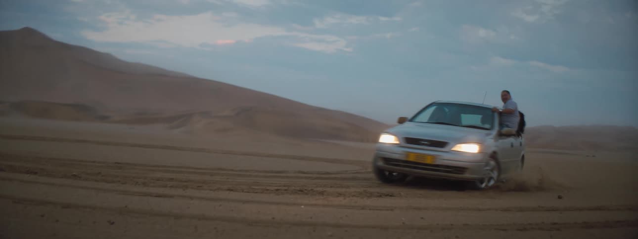 A car full of people spinning cookies in a desert while hanging out the car windows