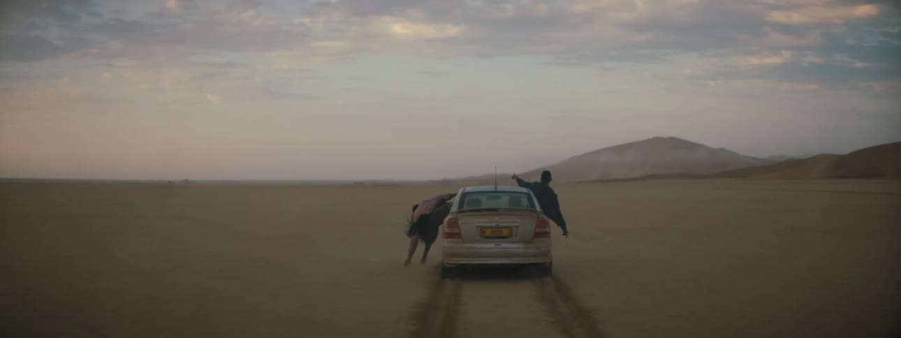 A group of people lean out the windows of a vehicle traveling offroad through the desert and run their fingers through the sand