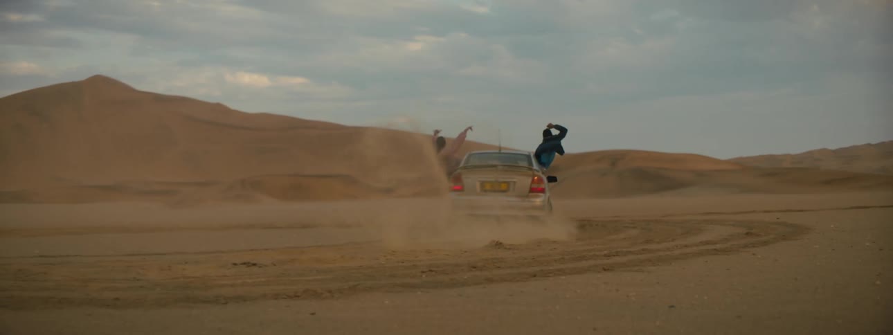 A car spinning cookies in a sandy desert with people hanging out the window