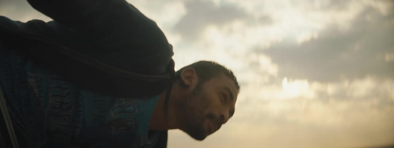 A man waves his arms and struggles to balance while laughing as he hangs halfway out of a vehicle driving through the desert