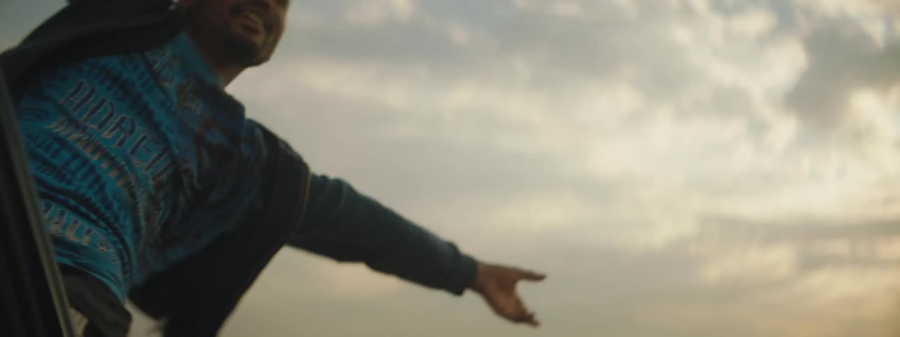 A man cheers as he leans far out of the window of a vehicle as it travels through the desert