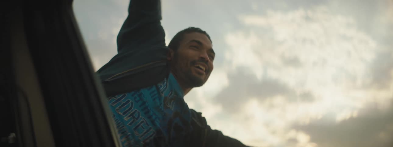 A man leans out of the window of a moving vehicle and cheers
