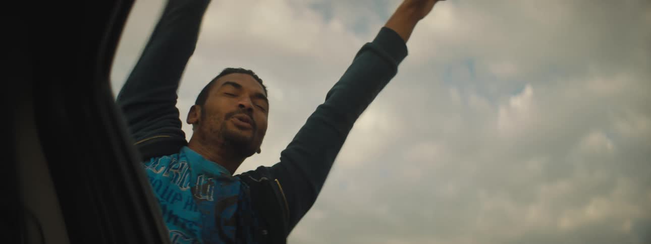 A young man laughs and yells as he hangs out of a car window