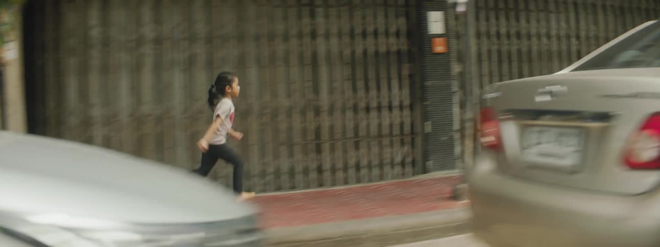 A young girl runs down an urban sidewalk by herself