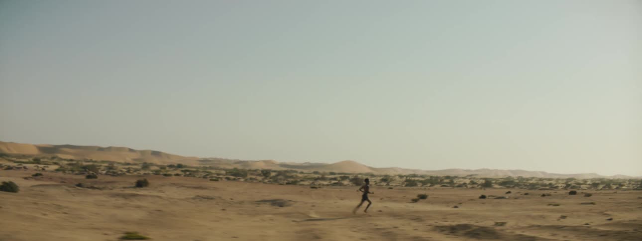 A person running in the desert with the sky and clouds in the background