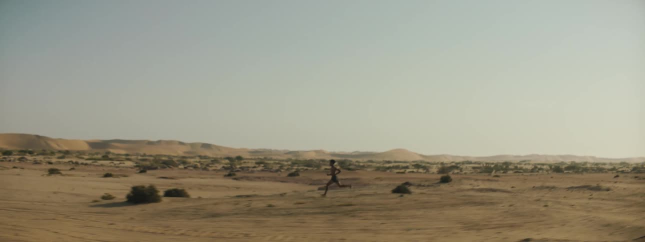 A shirtless man runs through the desert on a sunny day