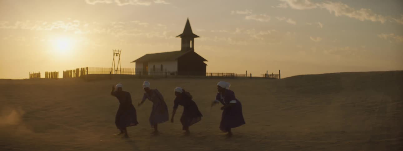 Four women in front of a church performing a dance in the sand