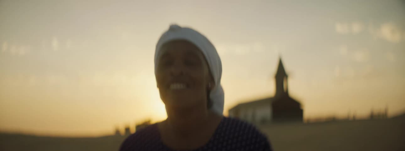 A black woman dancing happily in a field with a church in the background