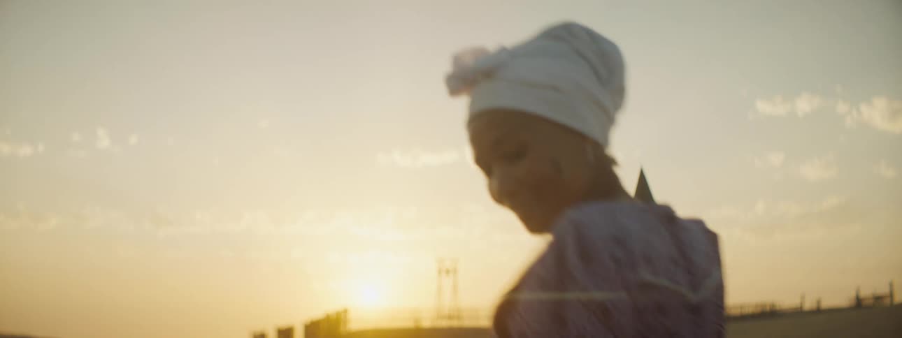 A woman with a dress dancing with a building the sky and clouds in the background