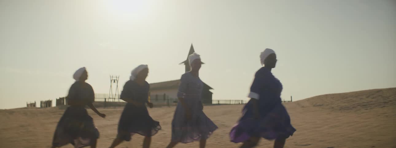 Women dancing outside with a building sky and clouds in the background