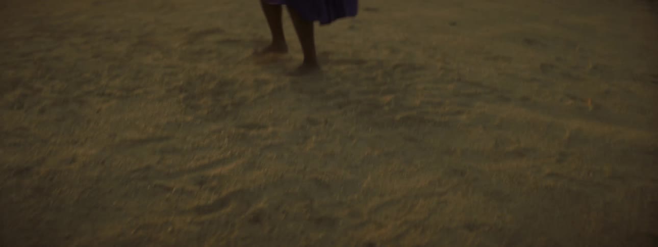 A barefoot woman in a purple dress dances in a field outside of a church in a rural area