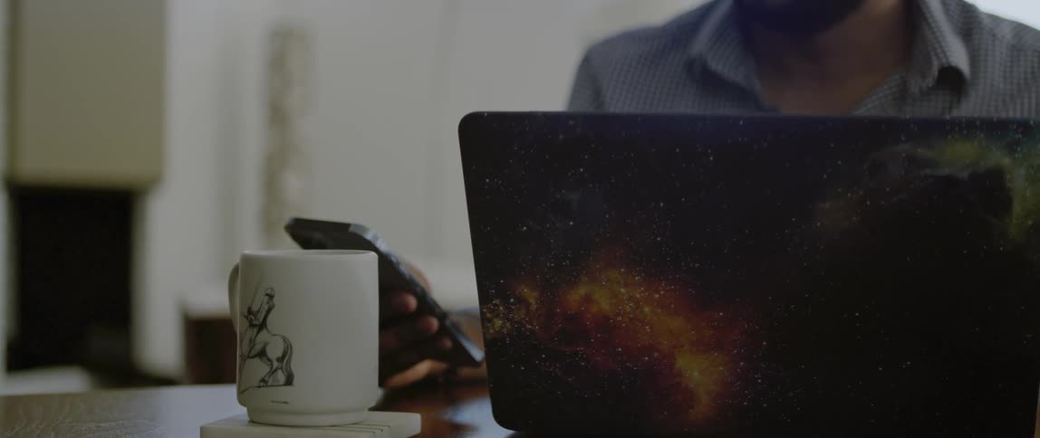 Man sitting in front of laptop turns smartphone over to check notification