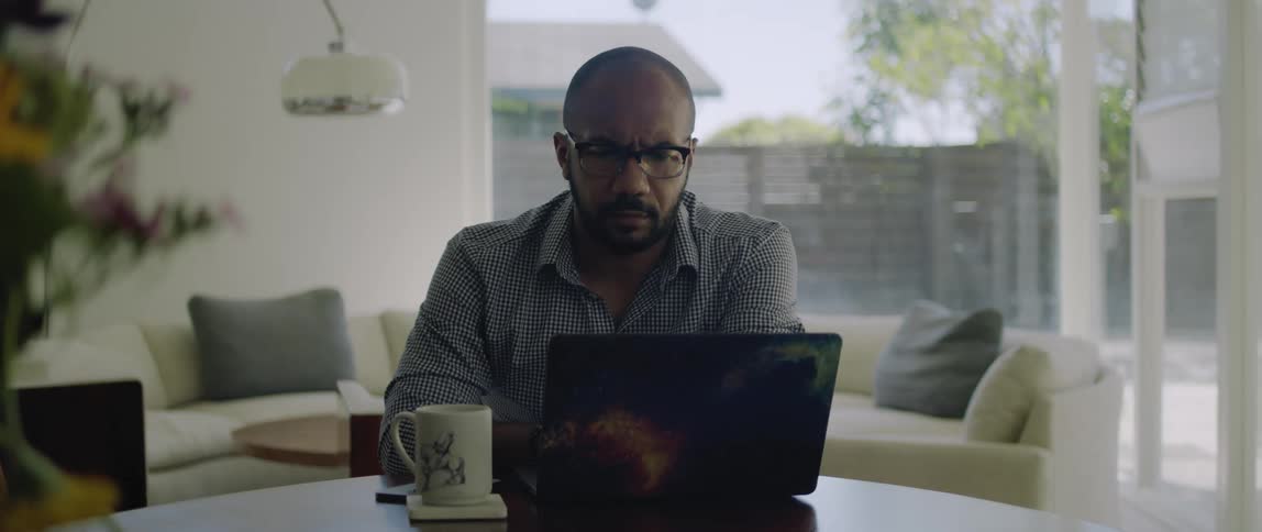 A man sits at home and looks at his computer with a confused look