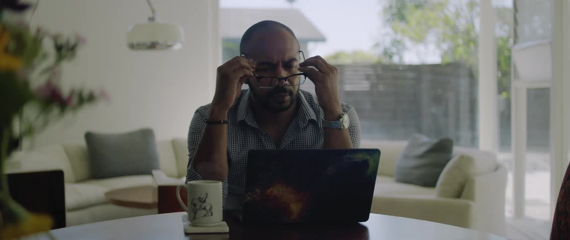 A man looking at his laptop and putting on glasses