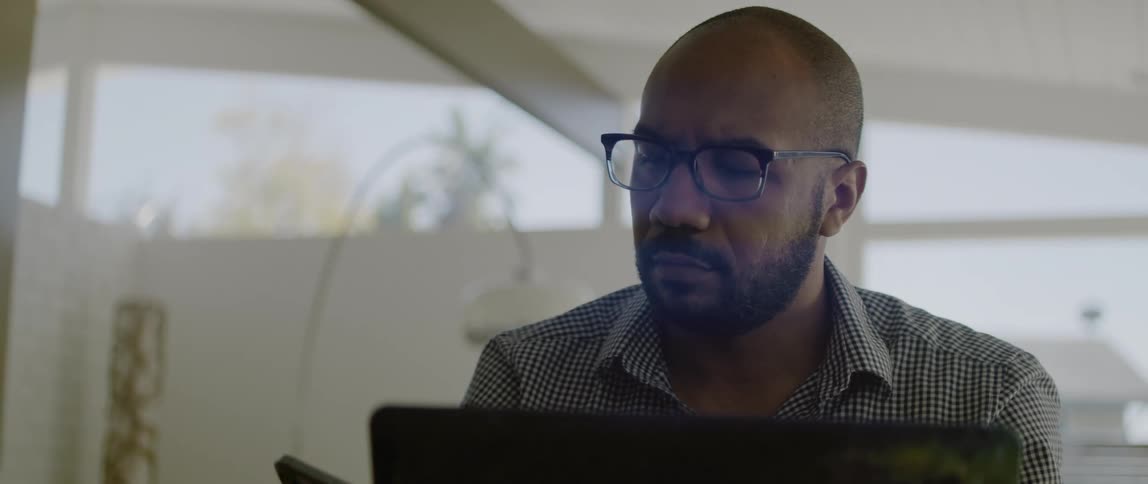 A man checks his smartphone while working on his laptop