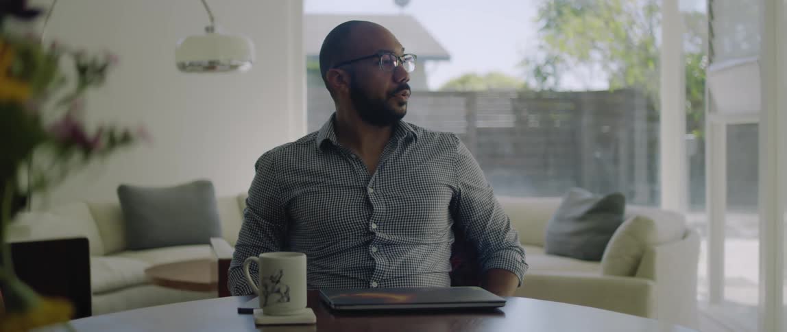 A man sitting in a room closes his laptop then takes off his glasses and rubs his eyes