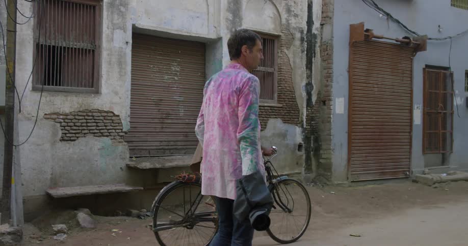 A man rides a bike past a man holding a camera