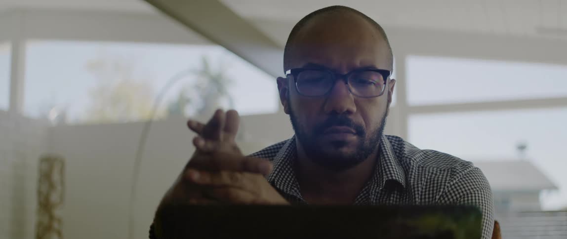 A man at home rubs his hands together and looks at his laptop