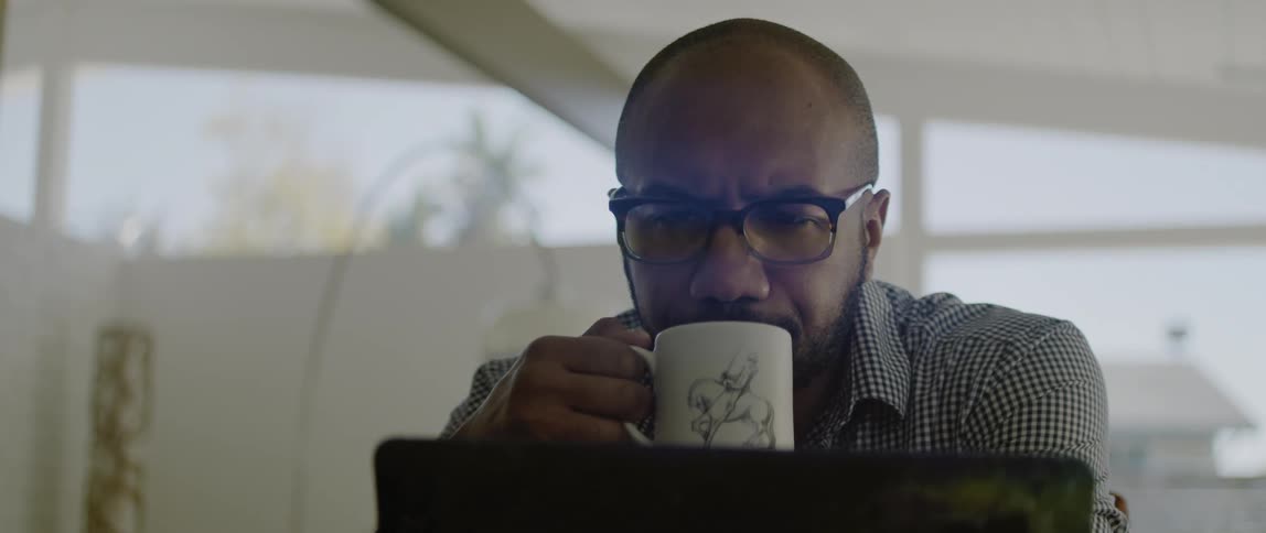 A man sits at his laptop at home and drinks coffee